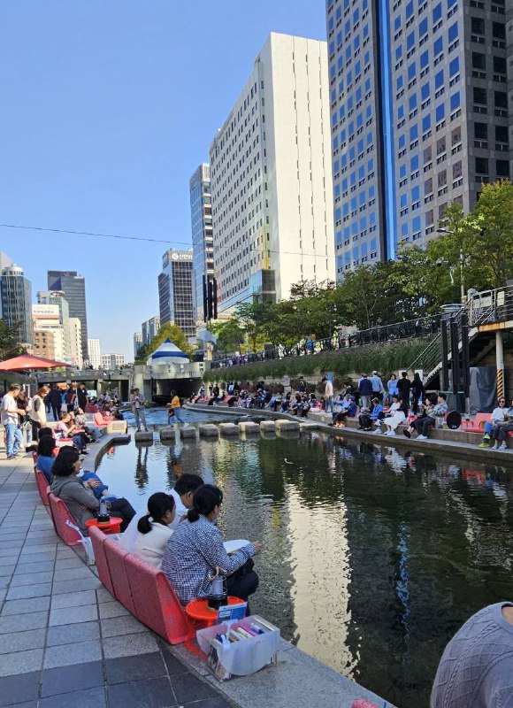 People relaxing by Cheonggyecheon Stream on benches and stepping stones
